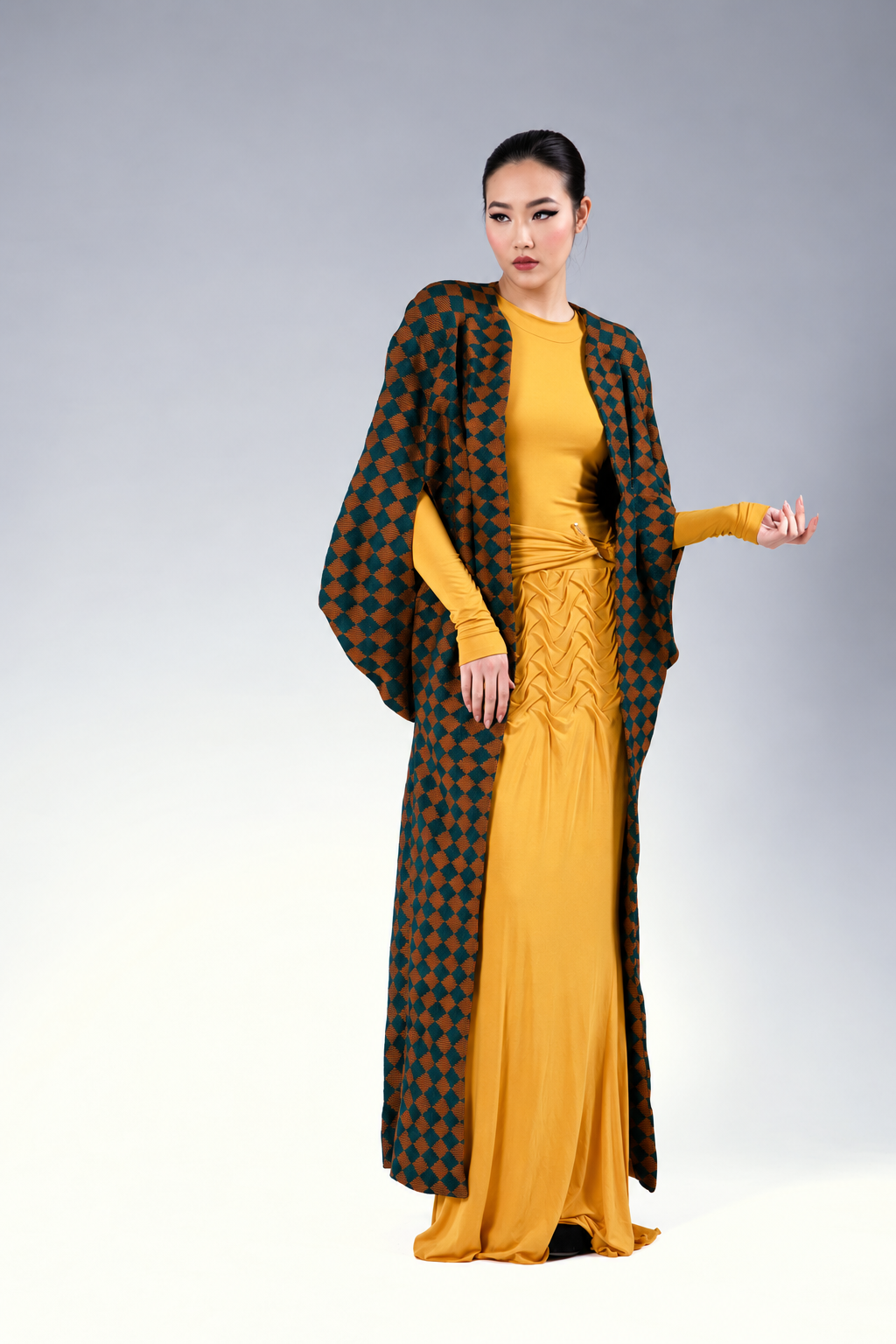 Model wearing the Anuke Aso-Oke cape in a dark green and copper-orange geometric pattern